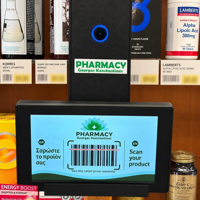 Η οθόνη του price checker στα ράφια του φαρμακείου με το μήνυμα «Σαρώστε το προϊόν σας / Scan your product» και ένα barcode.